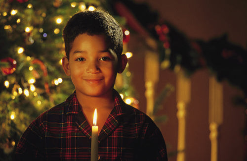 Boy holding lit candle by Christmas tree