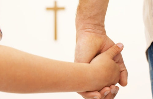Close-up of a father and son holding hands facing a crucifix