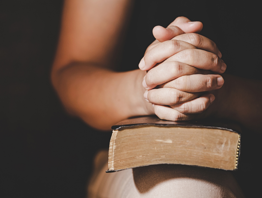 woman folding hands upon Bible to learn how to pray