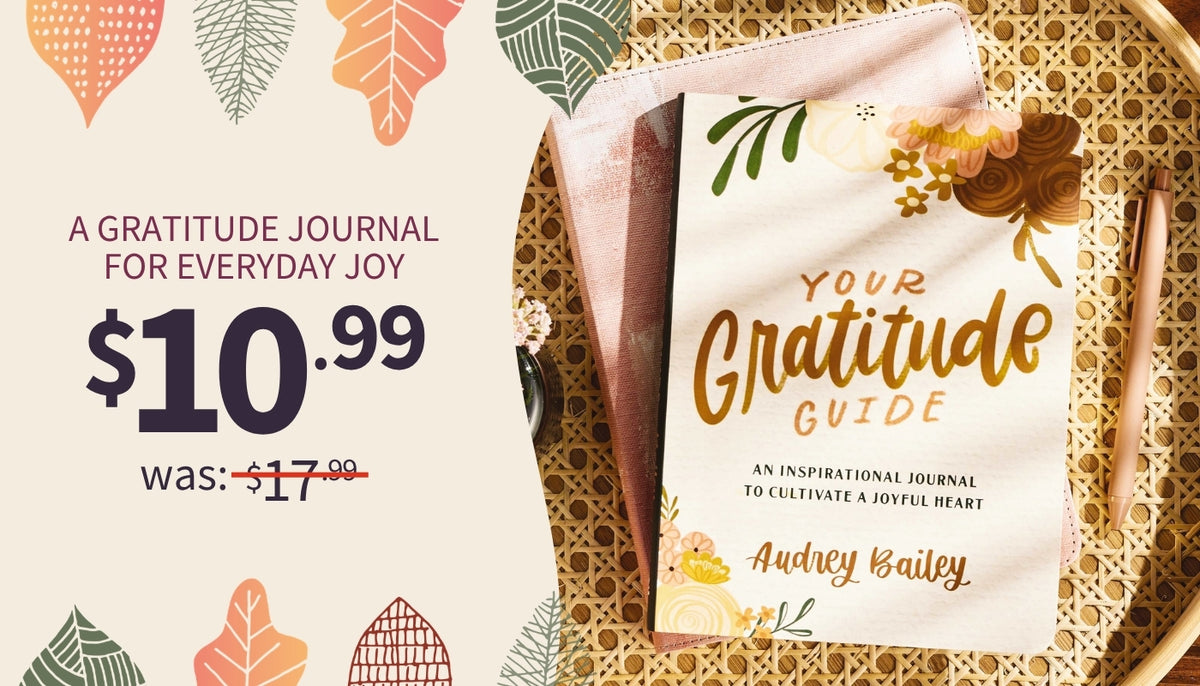Gratitude journal cover titled 'Your Gratitude Guide' by Audrey Bailey, shown on a woven tray with a pink notebook underneath. The left side includes promotional text reading 'A Gratitude Journal for Everyday Joy' and a price of $10.99 was $17.99.