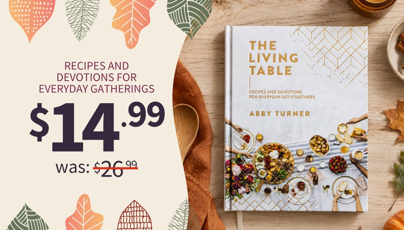 Recipes and Devotions for Everyday Gatherings - The Living Table cookbook by Abby Turner displayed on a wooden table next to a promotional price graphic on the left $14.99 was $26.99. 